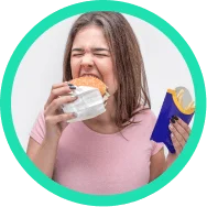 Mulher comendo um hambúrguer e segurando batatas fritas, simbolizando o controle do apetite e do desejo por alimentos calóricos.